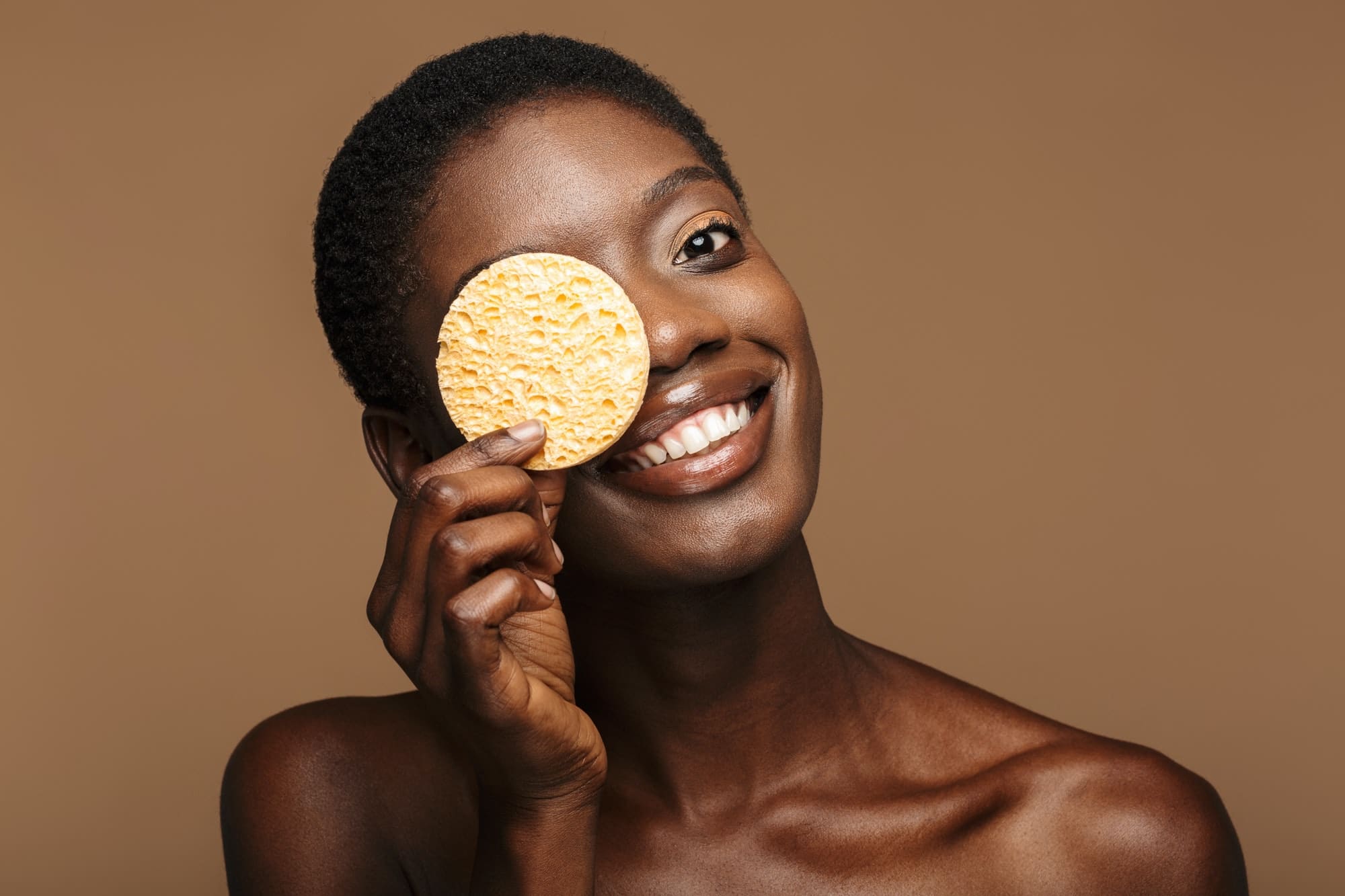 Beauty portrait of young half-naked african woman holding makeup sponge