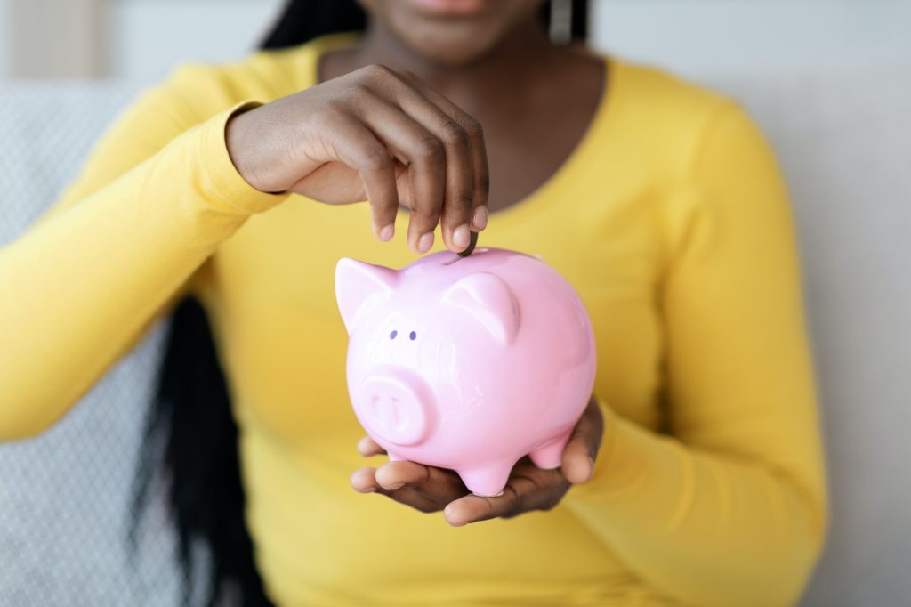 Money Savings. Closeup Of Black Woman Putting Coin To Piggy Bank