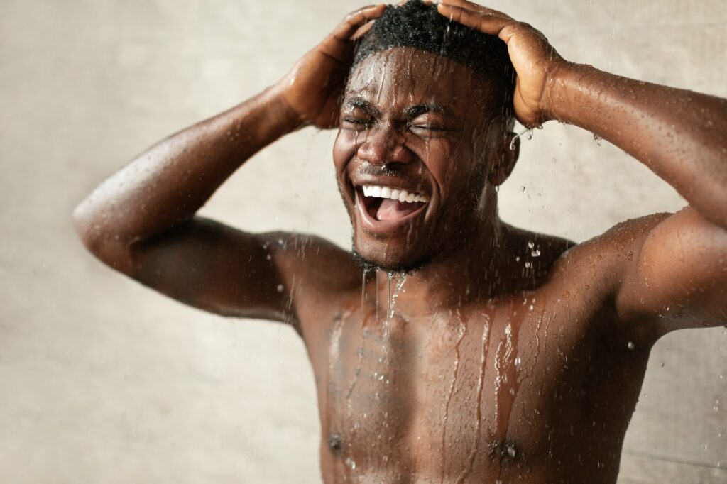 Black Man Enjoying Shower Standing With Eyes Closed In Bathroom