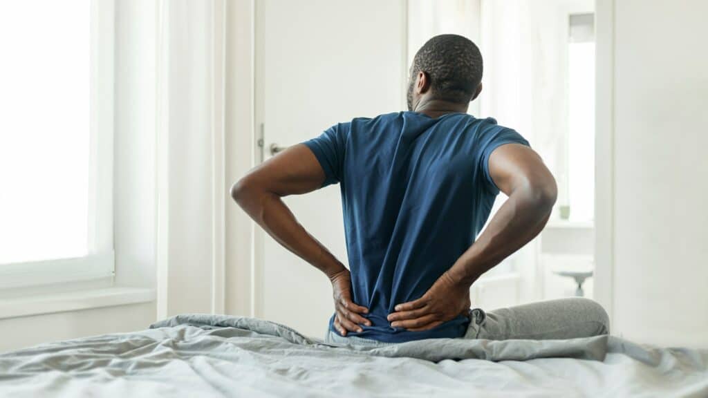 African Man Having Pain Touching Lower Back Sitting In Bedroom