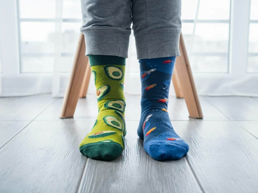 Two different artistic socks on feet, with avocados on the left and blue space on the right