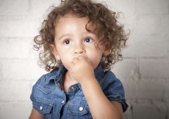 An adorable mixed race (caucasian and African American) 2 year old girl has a timid expression on her face.